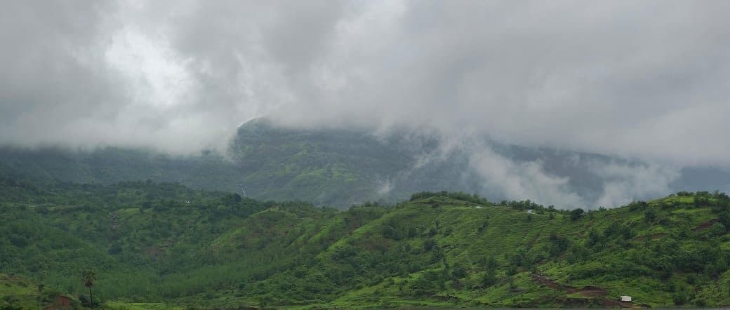 Cloud spilling over a dark Sahyadri ridge above a green valley.