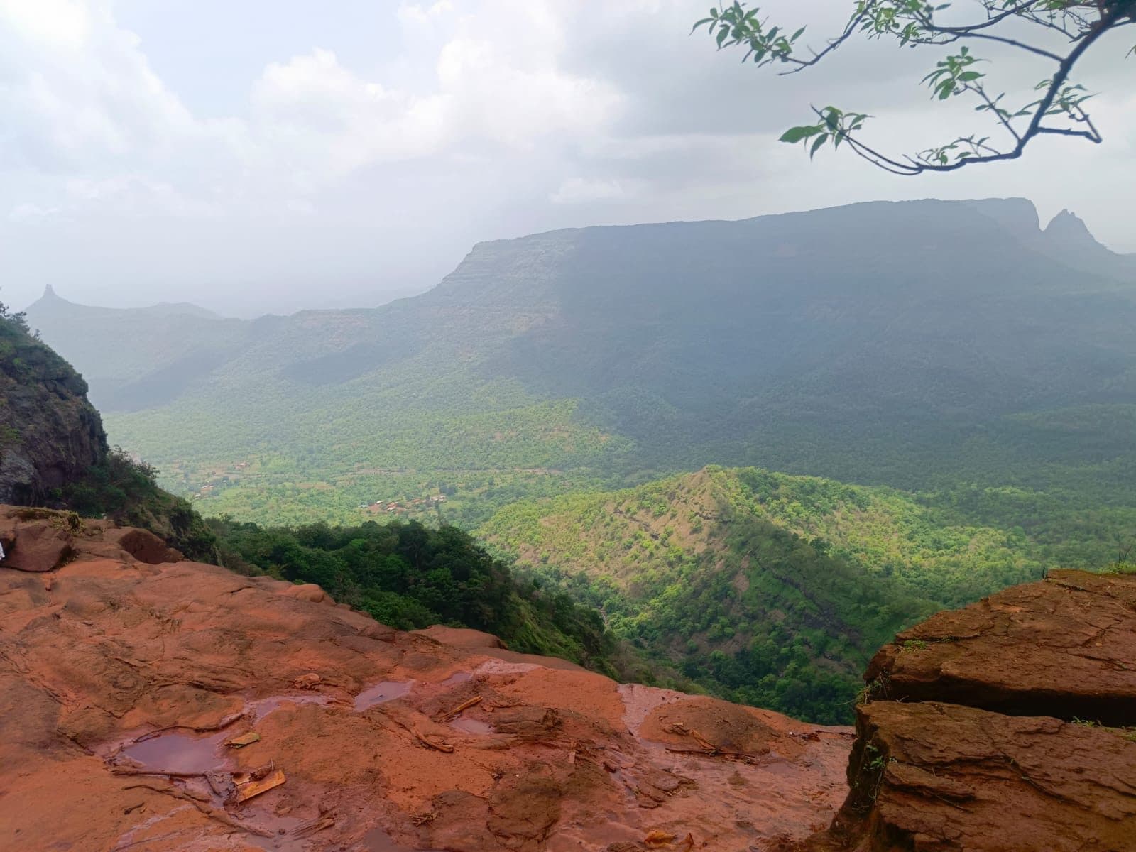 A wide plateau edge of red rock and grass under heavy monsoon cloud.