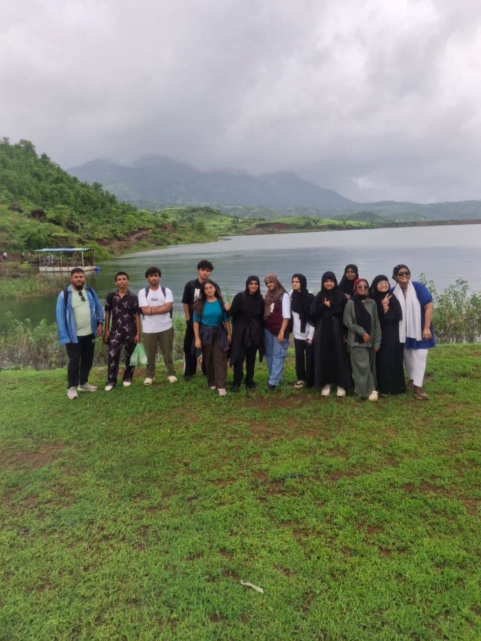 A trekking group standing together on grass beside a lake, hills behind them.