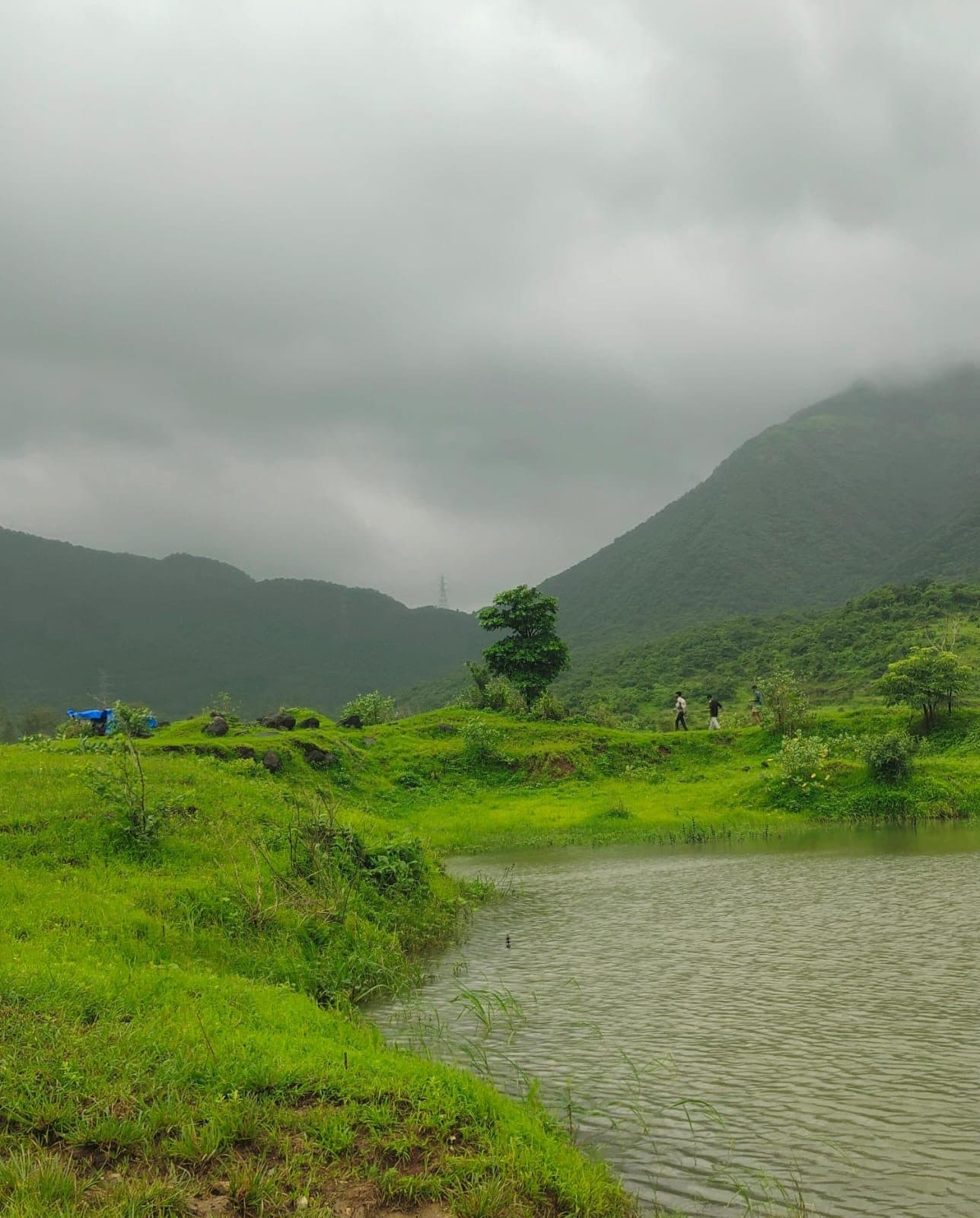 A still monsoon lake below a layered ridgeline under a heavy grey sky.
