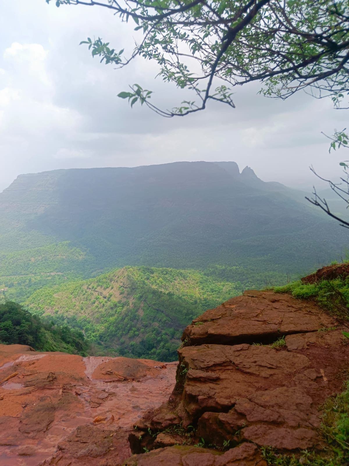 A red laterite rock ledge overlooking a deep green valley and distant ridgeline.